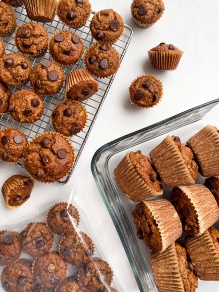 Regular sized and mini muffins on a wire rack, mini muffins in a ziploc bag and regular sized muffins in a glass container, ready for the freezer.