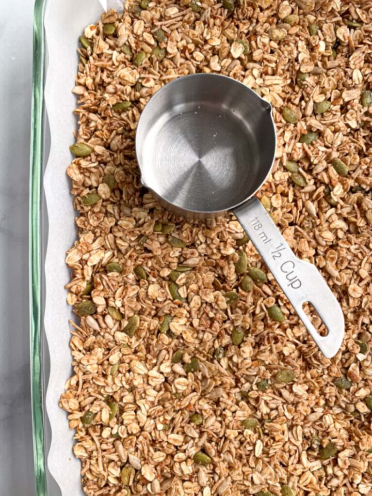 pan with unbaked granola pressed down using the back of a metal measuring cup