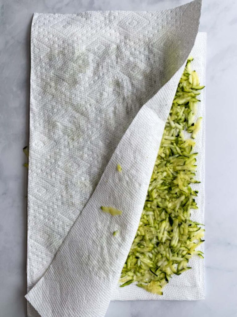 shredded zucchini in an even layer between two paper towels.