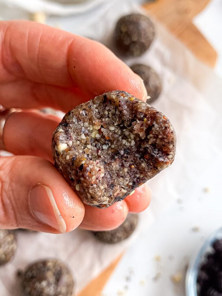 Hand holding a bitten blueberry energy ball showing the chewy texture inside