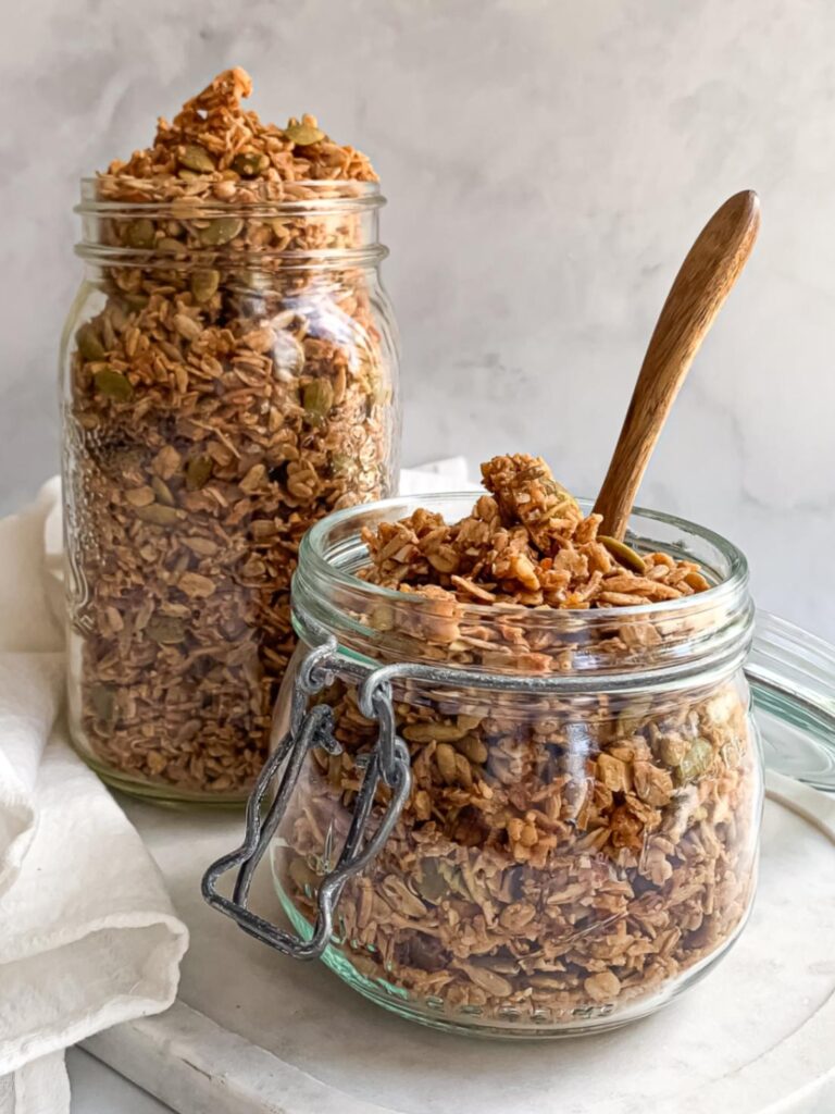 two jars of granola one short one tall with a wooden spoon coming out of the top of the short jar.