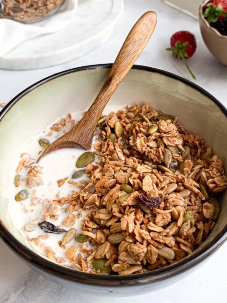 close up of a bowl with granola with milk and a wooden spoon in the milk.