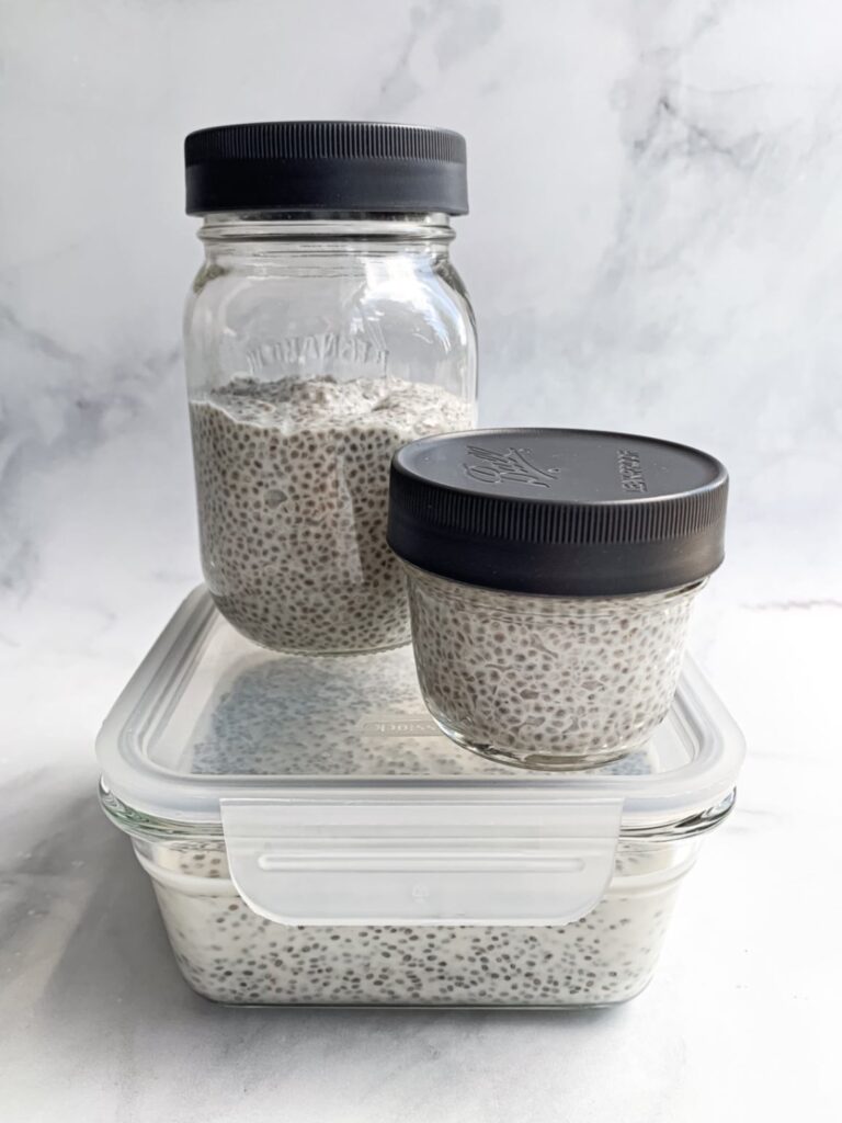 Glass storage container with lid, with one pint sized and one half pint sized mason jars with lids on top of it, all holding chia pudding inside.