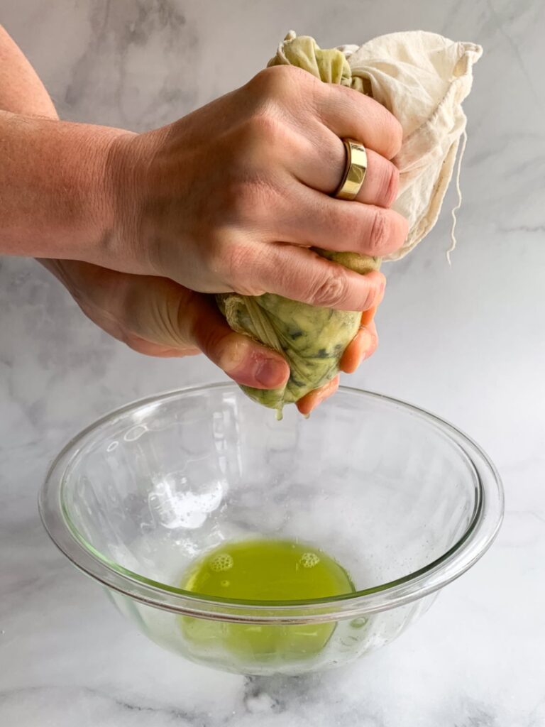 Hands squeezing a bag holding shredded zucchini over a bowl Removing excess moisture from the shredded zucchini before making almond flour muffins